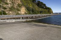 a long bridge is seen next to the lake and mountains near water with people riding bikes on it