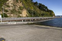 a long bridge is seen next to the lake and mountains near water with people riding bikes on it