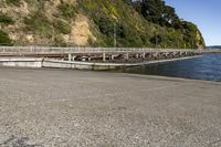 a long bridge is seen next to the lake and mountains near water with people riding bikes on it