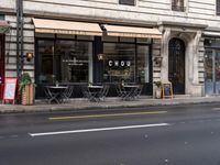 a city street with tables and chairs and an awning and windows that say chuc