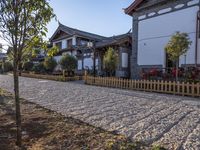 an old wooden fence sits on the gravel driveway of a building near a tree and bushes