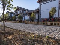 an old wooden fence sits on the gravel driveway of a building near a tree and bushes