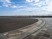 a brick walkway runs around a concrete park area next to a lake in the distance