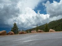 there is a black sign that is on a road with mountains in the background, on top of a hill near trees