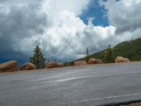 there is a black sign that is on a road with mountains in the background, on top of a hill near trees