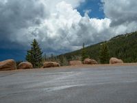 there is a black sign that is on a road with mountains in the background, on top of a hill near trees