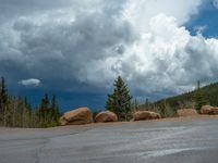 there is a black sign that is on a road with mountains in the background, on top of a hill near trees