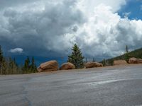 there is a black sign that is on a road with mountains in the background, on top of a hill near trees