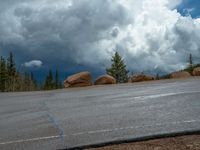 there is a black sign that is on a road with mountains in the background, on top of a hill near trees