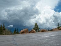 there is a black sign that is on a road with mountains in the background, on top of a hill near trees