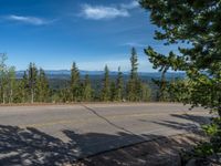 the mountains are visible in the distance from this wide, empty road, overlooking a wide landscape and forest