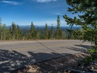 the mountains are visible in the distance from this wide, empty road, overlooking a wide landscape and forest