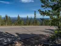 the mountains are visible in the distance from this wide, empty road, overlooking a wide landscape and forest