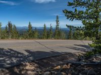 the mountains are visible in the distance from this wide, empty road, overlooking a wide landscape and forest