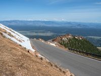 a man is riding his bike down a mountain road with snow and rocks in the background