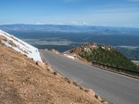 a man is riding his bike down a mountain road with snow and rocks in the background