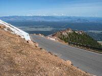 a man is riding his bike down a mountain road with snow and rocks in the background