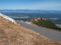 a man is riding his bike down a mountain road with snow and rocks in the background