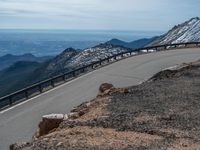 a snow covered road is near a very steep cliff on a clear day the wall is filled with snow and snow