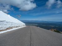 a snow covered road is near a very steep cliff on a clear day the wall is filled with snow and snow