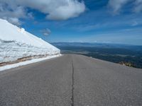 a snow covered road is near a very steep cliff on a clear day the wall is filled with snow and snow