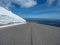 a snow covered road is near a very steep cliff on a clear day the wall is filled with snow and snow