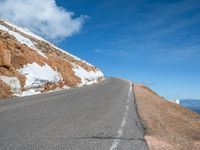 a man is riding his bike down a mountain road with snow and rocks in the background