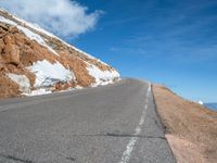 a man is riding his bike down a mountain road with snow and rocks in the background