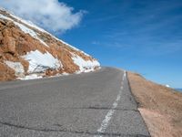 a man is riding his bike down a mountain road with snow and rocks in the background