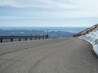 an empty road and a hill overlook the view of mountains and clouds and blue sky