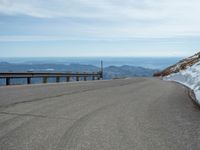 an empty road and a hill overlook the view of mountains and clouds and blue sky