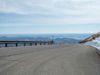 an empty road and a hill overlook the view of mountains and clouds and blue sky