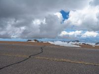 an empty road with snow and mountains in the back ground under cloudy skies on a sunny day