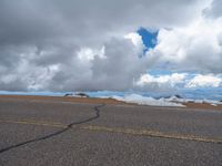 an empty road with snow and mountains in the back ground under cloudy skies on a sunny day