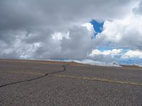 an empty road with snow and mountains in the back ground under cloudy skies on a sunny day