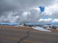 an empty road with snow and mountains in the back ground under cloudy skies on a sunny day