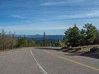 the mountains are visible in the distance from this wide, empty road, overlooking a wide landscape and forest