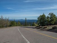 the mountains are visible in the distance from this wide, empty road, overlooking a wide landscape and forest