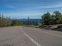 the mountains are visible in the distance from this wide, empty road, overlooking a wide landscape and forest