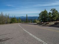 the mountains are visible in the distance from this wide, empty road, overlooking a wide landscape and forest