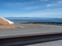 a man is riding his bike down a mountain road with snow and rocks in the background