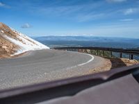 a man is riding his bike down a mountain road with snow and rocks in the background