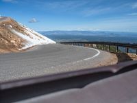 a man is riding his bike down a mountain road with snow and rocks in the background