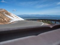 a man is riding his bike down a mountain road with snow and rocks in the background