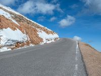 a man is riding his bike down a mountain road with snow and rocks in the background