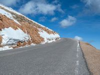 a man is riding his bike down a mountain road with snow and rocks in the background