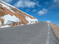 a man is riding his bike down a mountain road with snow and rocks in the background