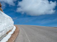 a snow covered road is near a very steep cliff on a clear day the wall is filled with snow and snow