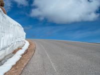 a snow covered road is near a very steep cliff on a clear day the wall is filled with snow and snow