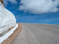 a snow covered road is near a very steep cliff on a clear day the wall is filled with snow and snow